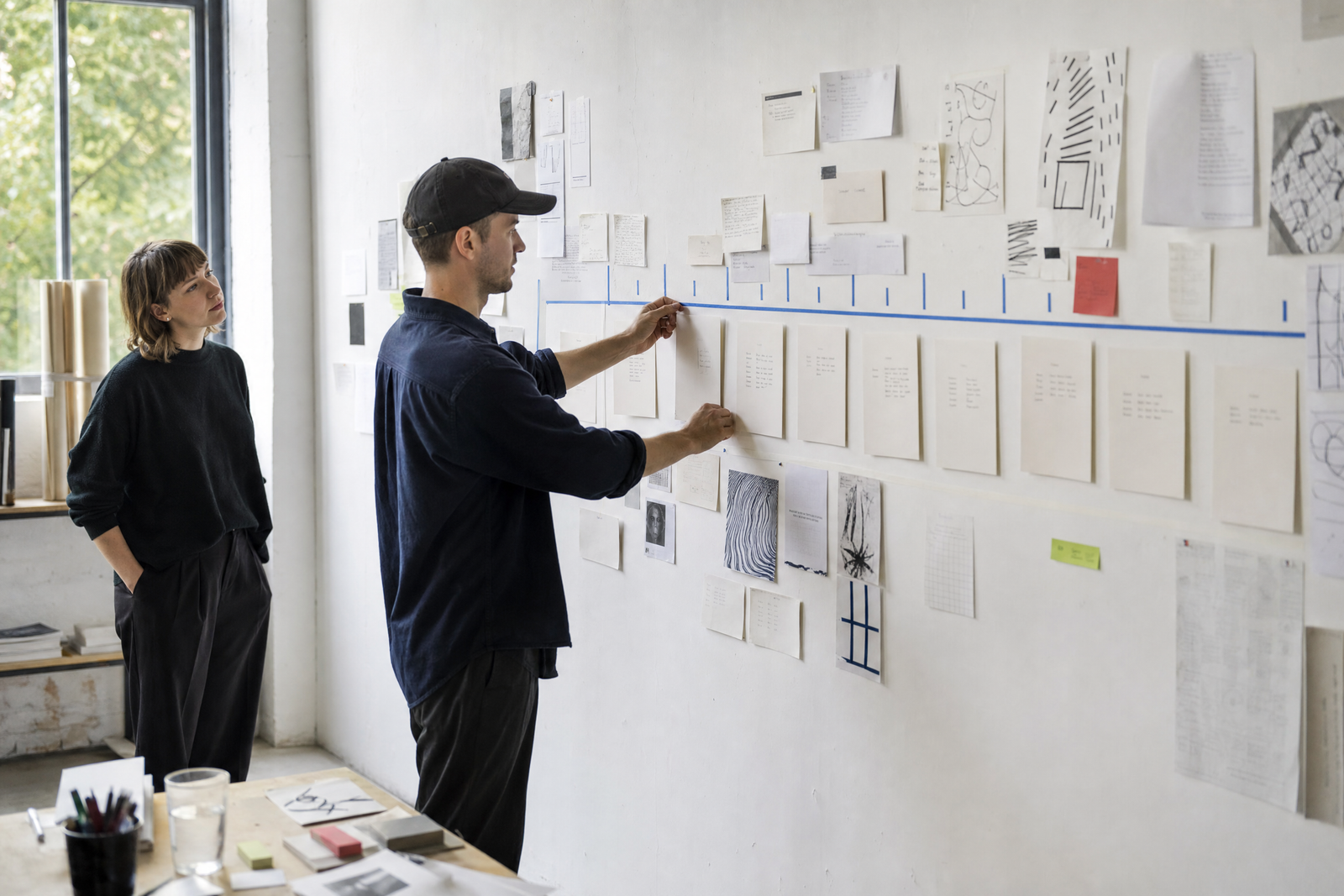 Zwei Kreativschaffende ordnen Arbeitsschritte an einer Studiowand